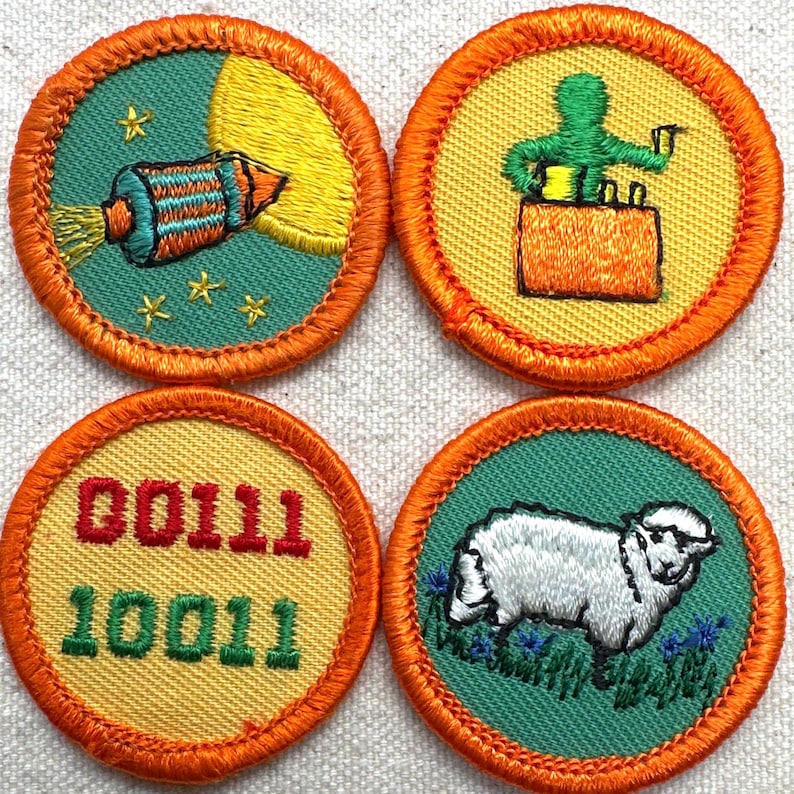 May include: Four round embroidered patches with orange borders. Designs include a rocket, a person on a box, binary code, and a sheep. The patches have green and yellow backgrounds with detailed stitching.