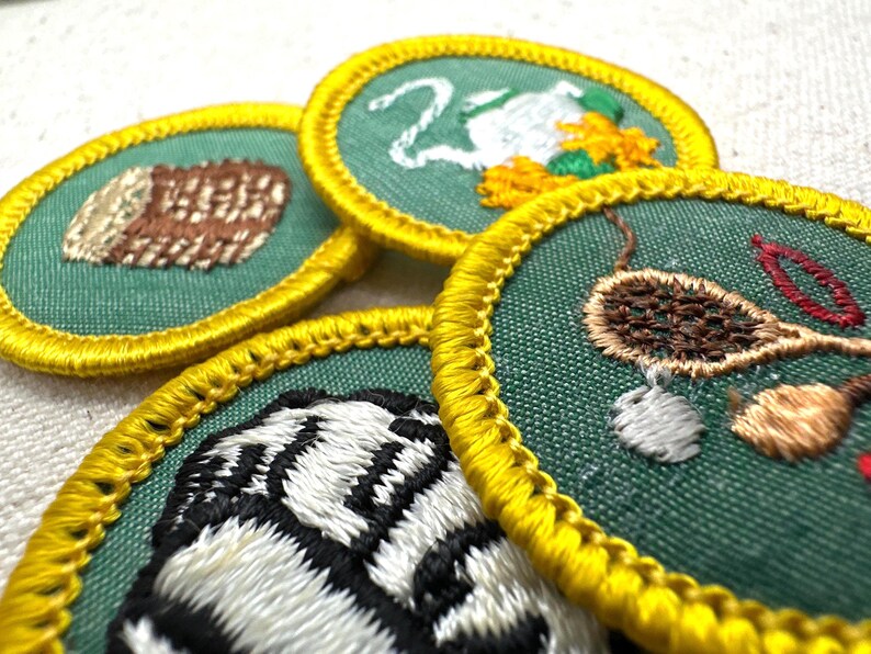 May include: Close-up of several embroidered patches with green backgrounds and yellow borders. The patches feature various designs, including a log, a swan, and a tiger stripe pattern. The patches are likely for a youth organization.