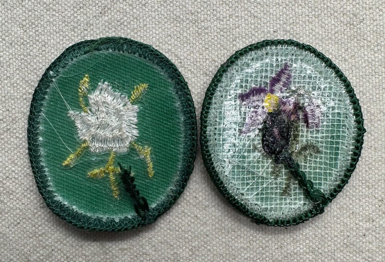 Pode incluir: Dois patches bordados com desenhos florais. Um apresenta uma flor branca com detalhes dourados sobre um fundo verde. O outro mostra uma flor roxa e amarela sobre um fundo de malha branca, ambos com bordas verdes.