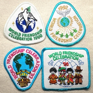 May include: Four embroidered patches with the words "World Friendship Celebration" and the years 1990, 1992, 1993, and 96. The patches feature images of a dove, globe, and children in traditional clothing. The patches have a white background with blue and green accents.