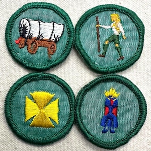 May include: Four embroidered patches with green borders. The patches feature a covered wagon, a person with a staff, a yellow cross, and a stylized figure. The patches are likely for a youth organization.