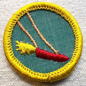 May include: Embroidered patch featuring a swing set design. The swing seat is red, the ropes are tan, and the frame is yellow. The patch has a yellow border and is set against a green background.
