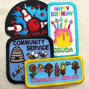 May include: A collection of embroidered patches with various designs. One patch features a bowling scene, another says "Happy Birthday" with a cake, and two others say "Community Service" with bees and other graphics. The patches are in various colors.