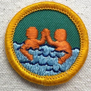 Puede incluir: Parche bordado con dos figuras naranjas chocando las manos en agua azul. Las figuras se destacan sobre un fondo verde, con un borde amarillo y costuras detalladas. Un art&iacute;culo &uacute;nico, hecho a mano.