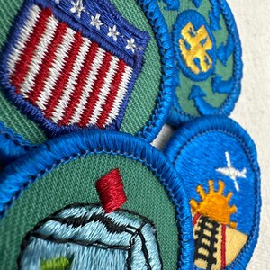 May include: Close-up of several embroidered patches with blue, green, red, white, and yellow details. One patch features a design of the American flag. Other patches have various designs, including a plane, sun, and abstract shapes.