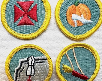 May include: Four embroidered patches with teal backgrounds and yellow borders. Designs include a red cross, an orange pumpkin with a white shoe, a sewing machine with a dress form, and a red swing with a yellow tassel.