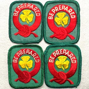 May include: Four green embroidered patches featuring the words "BE PREPARED" in red around a yellow shamrock. The patches are square with rounded corners and red detailing. The patches are for a scouting organization.