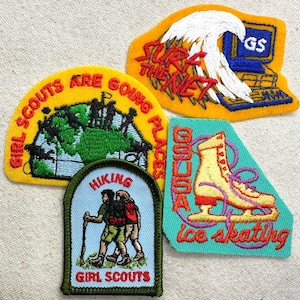 May include: A collection of Girl Scout patches. One patch features a globe with the text "Girl Scouts Are Going Places." Another shows a computer with the text "Surf the Net." Other patches depict hiking and ice skating.