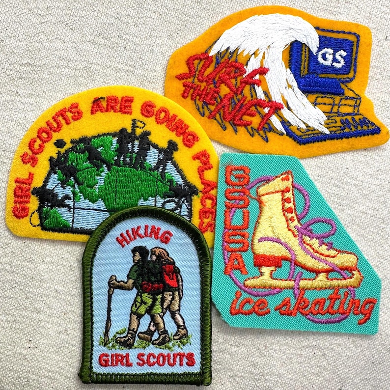 May include: A collection of Girl Scout patches. One patch features a globe with the text "Girl Scouts Are Going Places." Another shows a computer with the text "Surf the Net." Other patches depict hiking and ice skating.