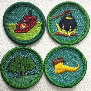 May include: Four round embroidered patches with green borders. The patches depict a brick structure with a fire, a pot over a fire, a tree, and a yellow boot. The patches are on a teal background.