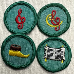 May include: Four round green embroidered patches. Two patches feature a red treble clef, one with a yellow accent. The other two patches depict a yellow shoe with a brown top and a scroll with black and white lines.
