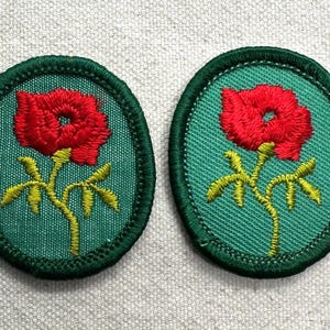 May include: Two oval-shaped embroidered patches featuring a vibrant red flower with a yellow stem and leaves centered on a teal background. Each patch is finished with a dark green stitched border, creating a clean and defined edge for application.
