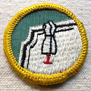 May include: Embroidered patch with a yellow border. The patch features a white dress form with black and red accents, set against a green and white background. The design is circular and appears to be a sewing or fashion-related emblem.