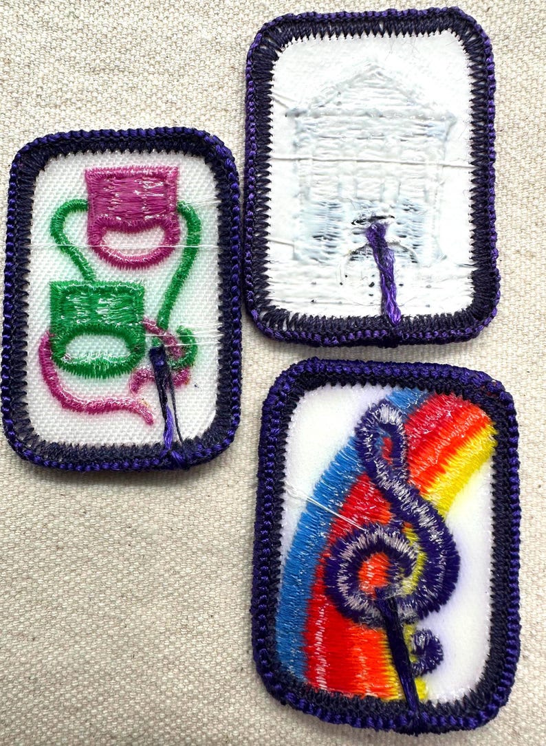 May include: Three embroidered patches with purple borders. One patch features a pink and green design, another depicts a white building, and the third showcases a rainbow and a treble clef.