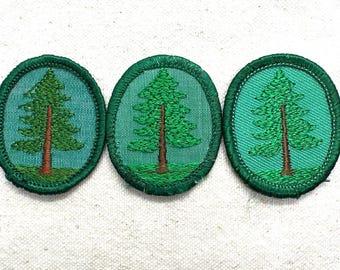 May include: Three oval-shaped patches with a green tree design. The tree has a brown trunk and green foliage, set against a teal background. Each patch is bordered with green stitching, and the patches are arranged horizontally.