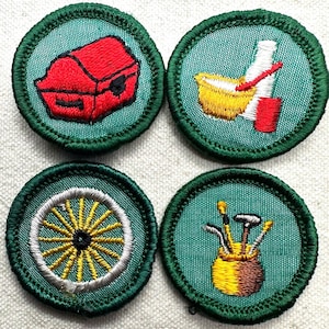 May include: Four embroidered patches with green borders and teal backgrounds. The patches feature a red treasure chest, a yellow bowl with a red utensil and white bottle, a yellow wagon wheel, and a golf bag with clubs.