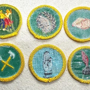 Pode incluir: Uma cole&ccedil;&atilde;o de seis patches redondos com bordas costuradas amarelas. Cada patch apresenta um design diferente em um fundo verde ou azul. Os designs incluem figuras, uma m&atilde;o e ferramentas, sugerindo um tema de habilidades ou atividades.