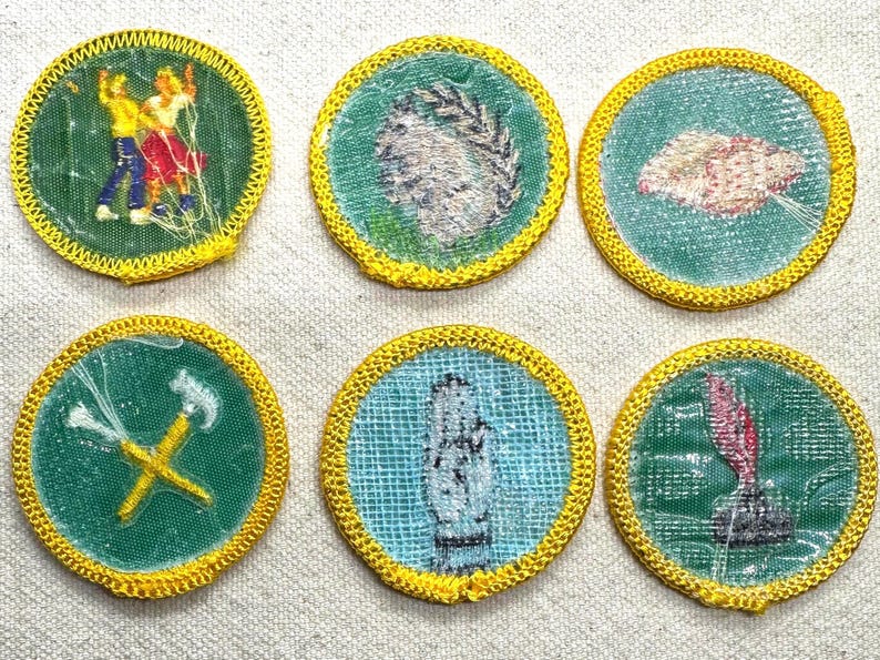 Pode incluir: Uma cole&ccedil;&atilde;o de seis patches redondos com bordas costuradas amarelas. Cada patch apresenta um design diferente em um fundo verde ou azul. Os designs incluem figuras, uma m&atilde;o e ferramentas, sugerindo um tema de habilidades ou atividades.