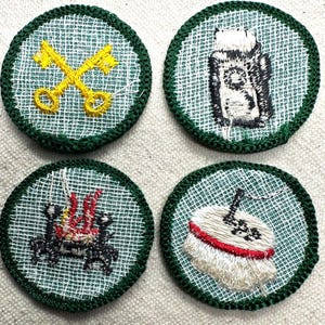 May include: Four embroidered patches with green borders. The patches feature various designs: crossed yellow keys, a black and white object, a red and black design, and a white object with a red band.