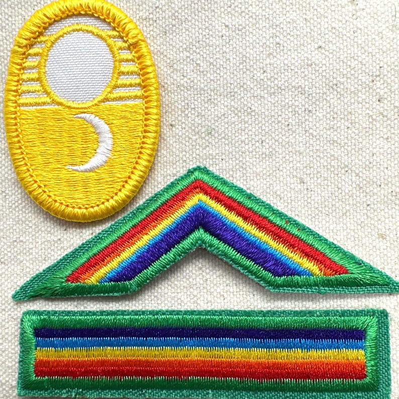 Puede incluir: Parches bordados en varias formas. Uno es ovalado con fondo amarillo y sol y luna creciente blancos. Otro es un gal&oacute;n verde con dise&ntilde;o de arco&iacute;ris. El &uacute;ltimo es un rect&aacute;ngulo verde con dise&ntilde;o de arco&iacute;ris.