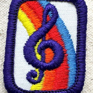 May include: Embroidered patch featuring a purple treble clef over a rainbow gradient of red, orange, yellow, and blue. The patch has a white background and a purple border, showcasing a vibrant design.
