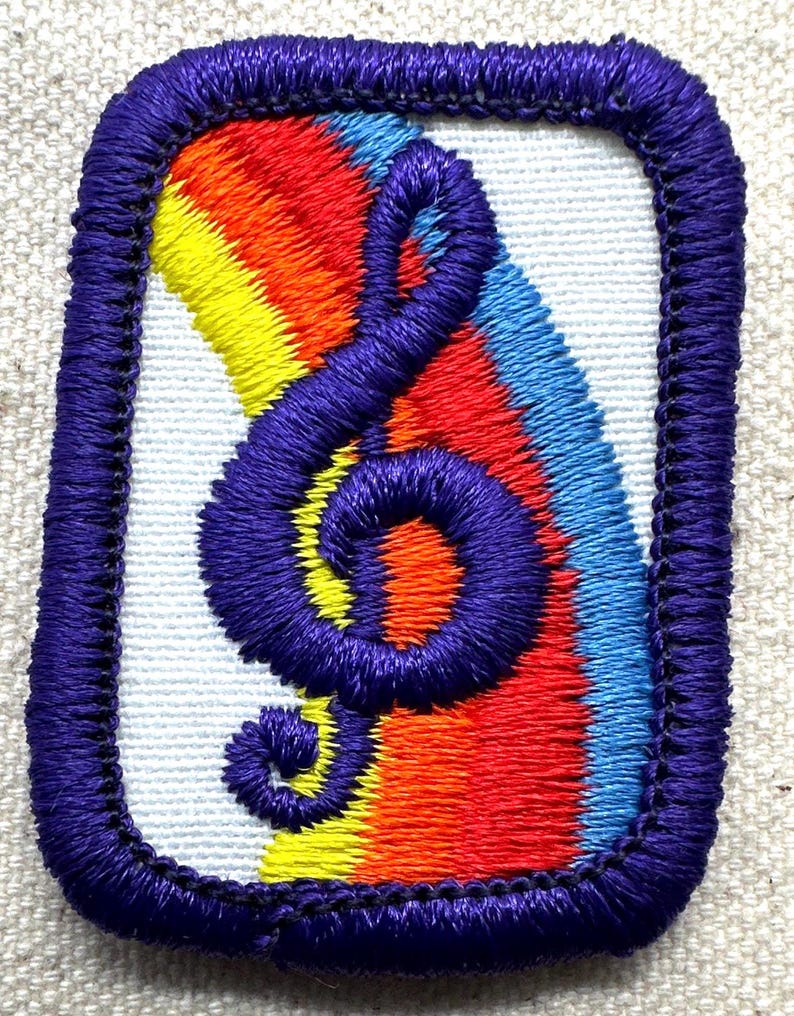 May include: Embroidered patch featuring a purple treble clef over a rainbow gradient of red, orange, yellow, and blue. The patch has a white background and a purple border, showcasing a vibrant design.