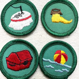 May include: Four embroidered patches with green borders. The patches feature various designs: a table with a white tablecloth, a yellow boot, a red chest, and a beach ball in the water. Each patch is circular and has a green background.