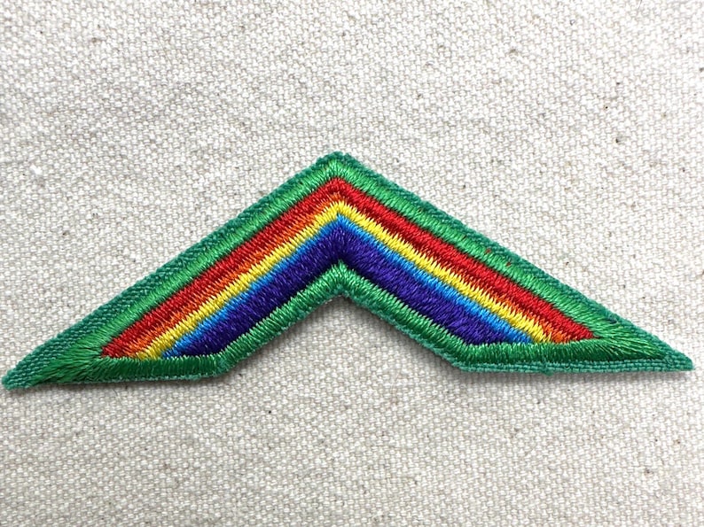 Puede incluir: Parche bordado con dise&ntilde;o de gal&oacute;n en colores del arco&iacute;ris: rojo, naranja, amarillo, verde, azul y morado. El parche tiene un borde verde y est&aacute; sobre un fondo texturizado blanquecino. Ideal para chaquetas, bolsos u otros art&iacute;culos de tela.