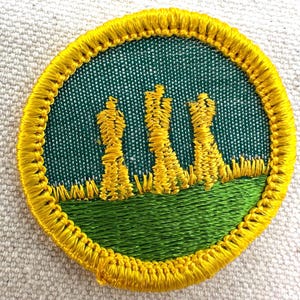 Pu&ograve; includere: Toppa ricamata con un design circolare. La toppa presenta uno sfondo verde con un bordo giallo. Il design include tre spighe di grano gialle su un campo verde. La toppa &egrave; probabilmente per un'organizzazione scout o simile.