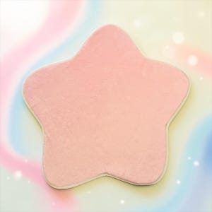 May include: A star-shaped pillow with a soft, light pink plush surface and a thin, light-colored border edge. The pillow features a smooth, uniform texture across its entire front face, maintaining a consistent five-pointed star silhouette.