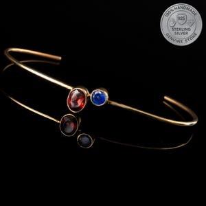 Peut inclure: Un bracelet doré avec un design incurvé, orné de trois pierres rouges et deux pierres bleues. Le bracelet est en argent sterling et est fait à la main. L'image comprend un tampon circulaire avec le texte "100% Handmade Sterling Silver Genuine Stone".