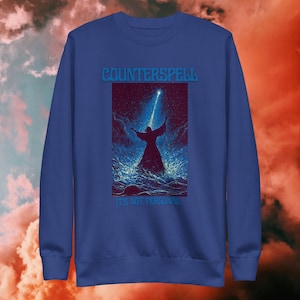 May include: Royal blue sweatshirt with the text "COUNTERSPELL" above an illustration of a figure in water reaching towards a beam of light. The text "IT'S NOT PERSONAL" is below the illustration.