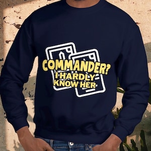 May include: Navy blue sweatshirt with the text "COMMANDER? I HARDLY KNOW HER" in yellow and white. The graphic is on two stylized card shapes. The sweatshirt is a long-sleeved crew neck.