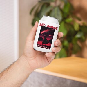 Könnte beinhalten: Weißer Getränkedosenkühler mit dem roten Text "Red Mage" über einer Grafik einer Figur, die einen roten Zauber wirkt. Der Text "BECAUSE FIRE IS HOT" steht darunter. Der Kühler wird in einer Hand gehalten.