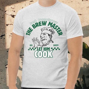 Pode incluir: T-shirt cinza claro com um design verde e preto. O design diz "The Brew Master" com uma ilustração de chef e o texto "Let Him Cook". A camisa também tem o texto "Jank Connoisseur" e "Est. 2025".