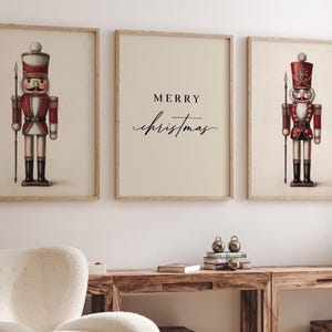 May include: Three framed prints featuring a Christmas theme. Two prints depict vintage-style nutcracker soldiers in red, white, and black. The center print has the words "MERRY Christmas" in elegant script on a cream background.