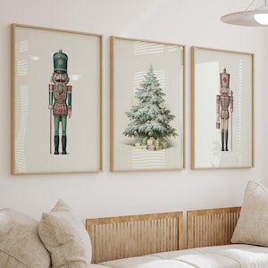 Puede incluir: Tres láminas de pared enmarcadas sobre un sofá beige. La lámina de la izquierda muestra un cascanueces verde, la central un árbol de Navidad decorado con regalos y la de la derecha una figura de cascanueces en rojo y dorado.