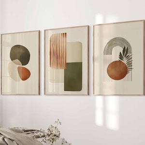 May include: A set of three framed wall art prints featuring abstract geometric shapes and line art in shades of olive green, terracotta, and cream. The first print shows overlapping circles, the second vertical lines, and the third an arch.