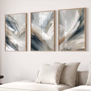 Pode incluir: Três impressões de arte de parede retangulares com pinceladas abstratas em tons de azul ardósia, bege, branco e cinza carvão. Cada peça está emoldurada em madeira clara, exibindo texturas de tinta em camadas sobre a tela.