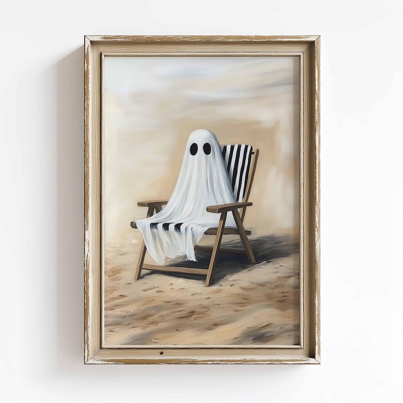 K&ouml;nnte beinhalten: Gerahmtes Kunstwerk, das eine wei&szlig;e Geisterfigur mit schwarzen Augenl&ouml;chern zeigt, die &uuml;ber einem Holzstrandstuhl mit schwarz-wei&szlig; gestreiftem Stoff drapiert ist. Das Kunstwerk ist an einem sandigen Strand mit hellem beigen Himmel angeordnet.