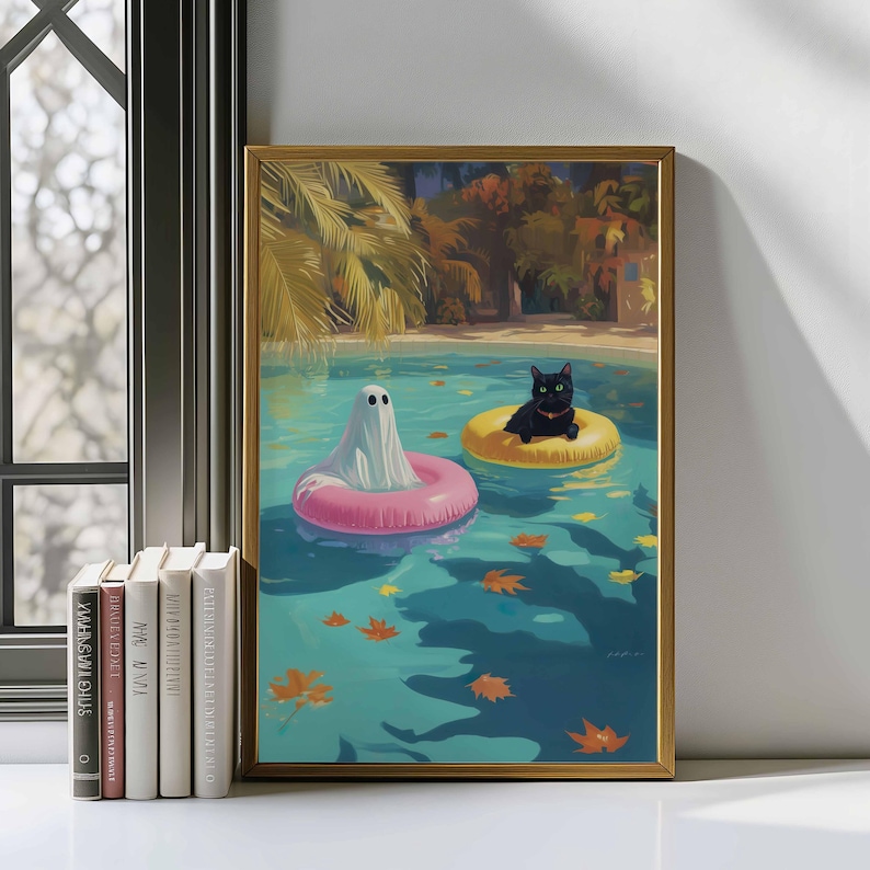 May include: A framed art print depicts a ghost and a black cat floating in a swimming pool on inflatable rings. The ghost is in a pink ring, and the cat is in a yellow ring. The pool has a turquoise hue, with autumn leaves floating on the surface.