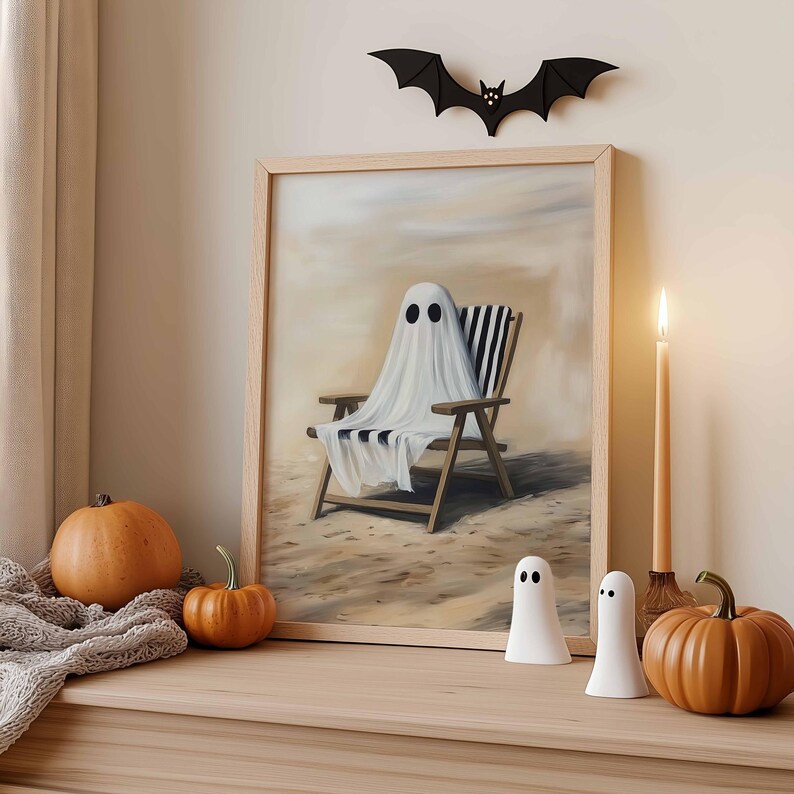 K&ouml;nnte beinhalten: Ein gerahmtes Kunstwerk zeigt einen Geist, der sich an einem Strand entspannt. Die Szene wird durch Halloween-Dekorationen erg&auml;nzt: K&uuml;rbisse, Geisterfiguren, eine Fledermaus-Silhouette und eine brennende Kerze, die eine gem&uuml;tliche Atmosph&auml;re schafft.