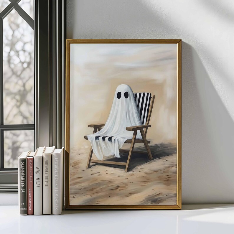 K&ouml;nnte beinhalten: Ein gerahmter Kunstdruck zeigt einen wei&szlig;en Geist, der &uuml;ber einem Holz-Strandstuhl mit schwarz-wei&szlig; gestreiftem Stoff drapiert ist. Das Kunstwerk befindet sich an einem Sandstrand mit hellem Himmel. Der Rahmen ist goldfarben.