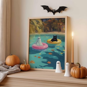 May include: A framed print depicts a ghost and a black cat floating in a pool on inflatable rings. A black bat decorates the wall above the print. Pumpkins, ghost figurines, and a lit candle complete the Halloween-themed display.
