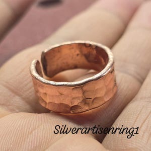 May include: A copper-colored adjustable ring with a hammered texture. The ring is open at the top and sits on a hand. The text "Silverartisenring1" is visible at the bottom of the image.