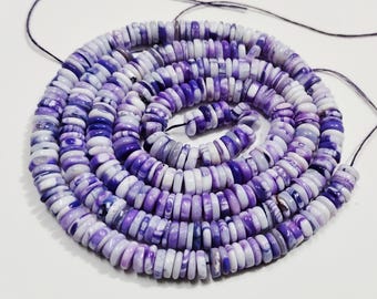 May include: A strand of purple and white disc-shaped beads. The beads are strung together on a black string, forming a spiral. The beads have a marbled appearance, with variations in color and pattern.