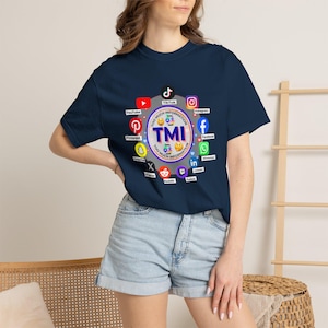 May include: Navy blue t-shirt featuring a circular graphic with the text "TMI" surrounded by social media logos, including YouTube, TikTok, and Instagram. The phrase "TOO MUCH INFORMATION" is also displayed. A casual, everyday wear tee.