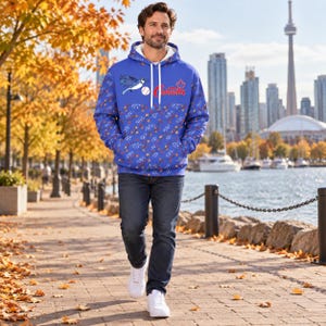 Può includere: Una felpa con cappuccio blu con fodera interna bianca, una grafica raffigurante una ghiandaia azzurra, una palla da baseball e la scritta rossa Canada. Il capo è decorato con un motivo ripetuto di piccole foglie d'acero e rami sul fondo.