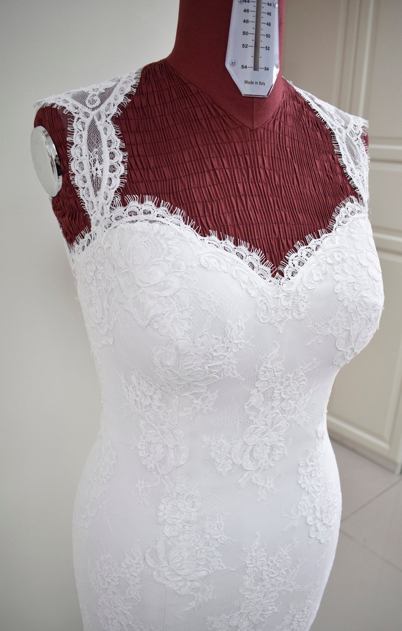 Puede incluir: Un vestido de novia de encaje blanco con escote de coraz&oacute;n y silueta ajustada. El vestido est&aacute; en un maniqu&iacute;.