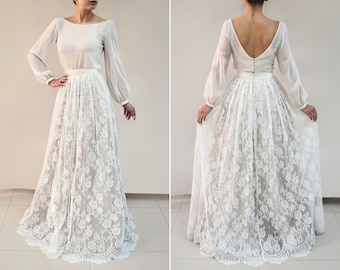 May include: A white lace wedding skirt with a fitted waist and a flowing, full skirt. The skirt is made of delicate lace with a floral pattern. The skirt is paired with a white long-sleeved blouse with a scoop neckline.